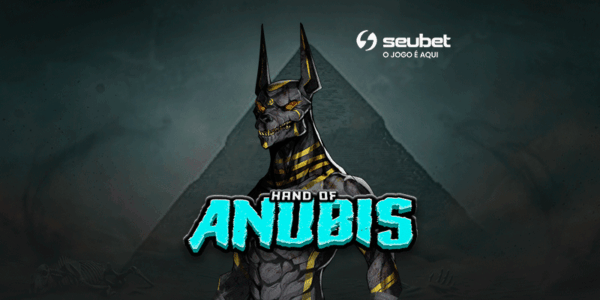 Banner promocional para análise do jogo de cassino online Hand of Anubis na plataforma Seubet. No centro, destaca-se a figura imponente e sombria do deus egípcio Anubis, representado com cabeça de chacal, olhos brilhantes e detalhes dourados no corpo musculoso. Logo abaixo, o título "HAND OF ANUBIS" aparece em letras estilizadas na cor ciano vibrante. O cenário de fundo apresenta uma pirâmide sob uma atmosfera escura, densa e enevoada em tons de cinza e preto. No topo central, encontra-se o logotipo da Seubet. Arte focada em reviews de caça-níqueis (slots) com temática de mitologia egípcia e estilo dark.