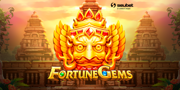 Banner promocional do jogo de cassino online Fortune Gems na plataforma Seubet. No centro da arte, destaca-se uma imponente máscara dourada de uma figura mitológica adornada com pedras preciosas vermelhas. Logo abaixo, o título "Fortune Gems" brilha em letras douradas com gemas verde e azul incrustadas. O cenário de fundo exibe majestosas ruínas de templos de pedra antigos, envoltos por uma vegetação tropical sob a luz alaranjada de um pôr do sol. Nas laterais, flutuam elementos desfocados do jogo, como um símbolo "WILD" à esquerda e um quadro de multiplicador "SUPER WIN" à direita. No topo, encontra-se o logotipo da Seubet. Arte focada em jogos de caça-níqueis (slots) com temática de exploração e tesouros.